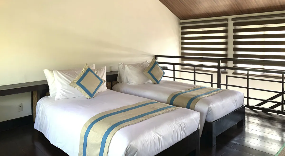 The two single beds on the upper floor, beside the mezzanine railing and under the timber pitch