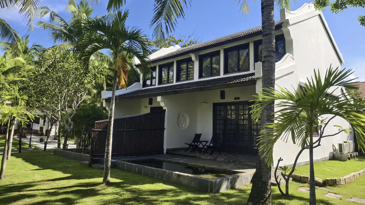 The duplex villa from the garden: two storeys, a tiled roof and the sheet of water in front of the porch