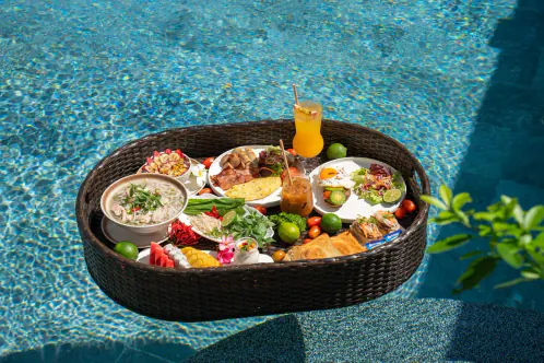 A breakfast tray floating in the pool, with cut fruit, phở and a juice