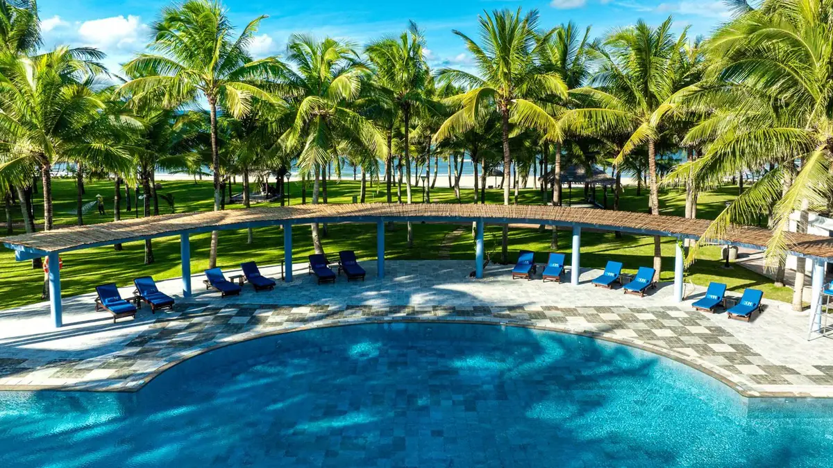 The resort pool from above, with its reed pergola, the loungers, the coconut grove and the beach beyond