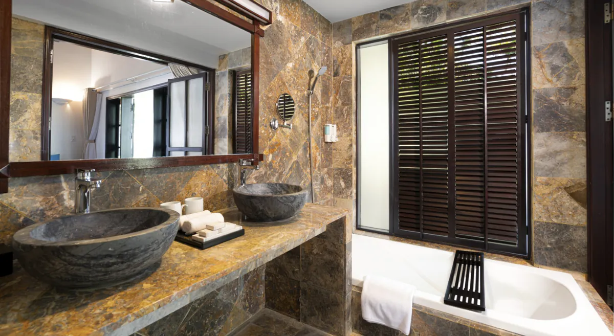 Baño con dos lavabos de piedra sobre encimera de mármol, espejo de madera, bañera y contraventanas de lamas