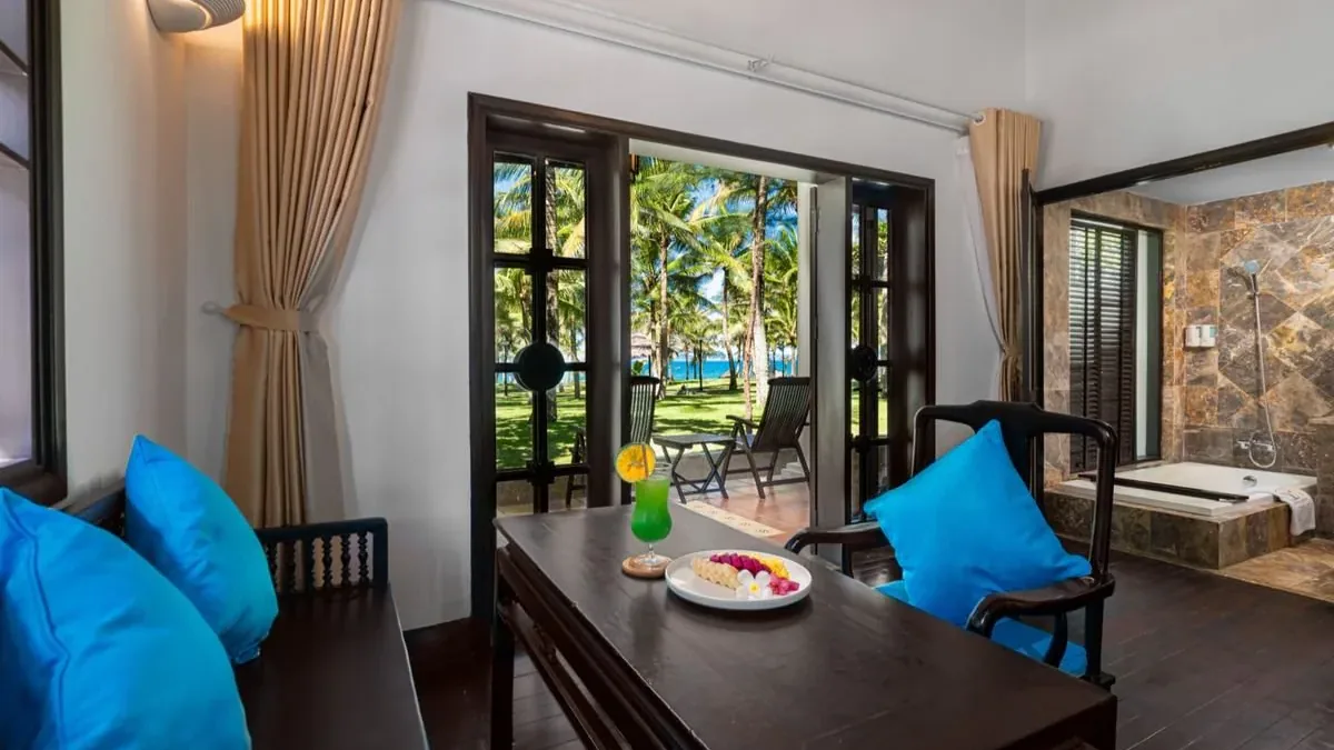 A villa's living and dining area with the doors open onto the garden and the sea, the stone bathroom with its bath to the right