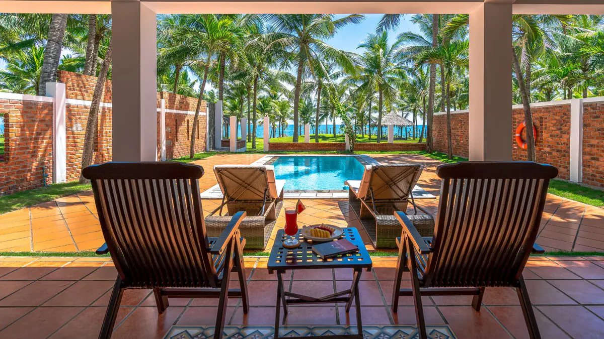From the porch of a villa at Le Belhamy: two teak chairs, the private pool, the brick wall and the sea among the coconut palms