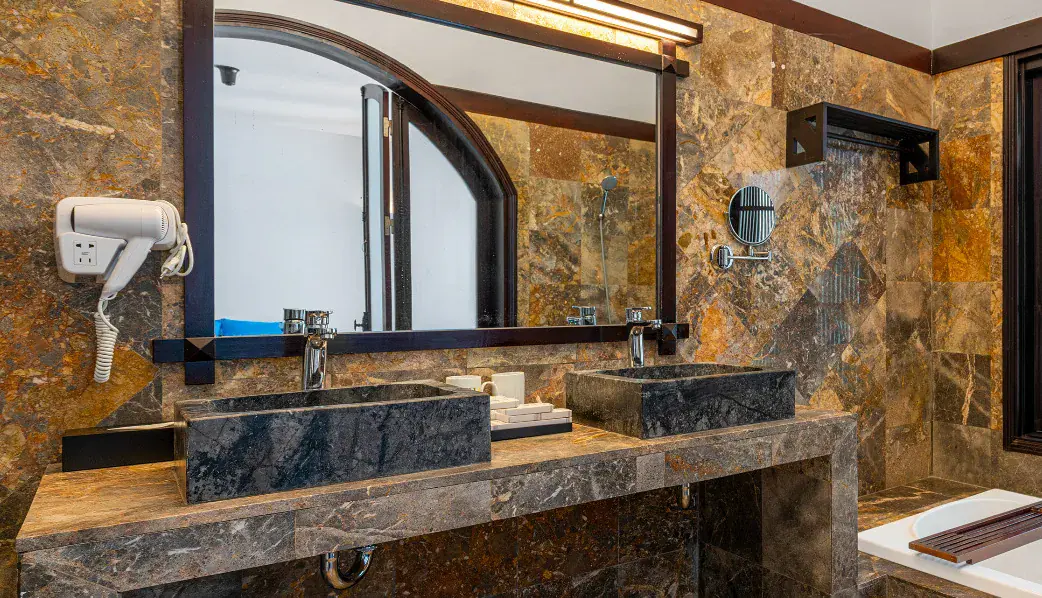 Baño de mármol con dos lavabos de piedra tallada, espejo corrido y la ducha detrás