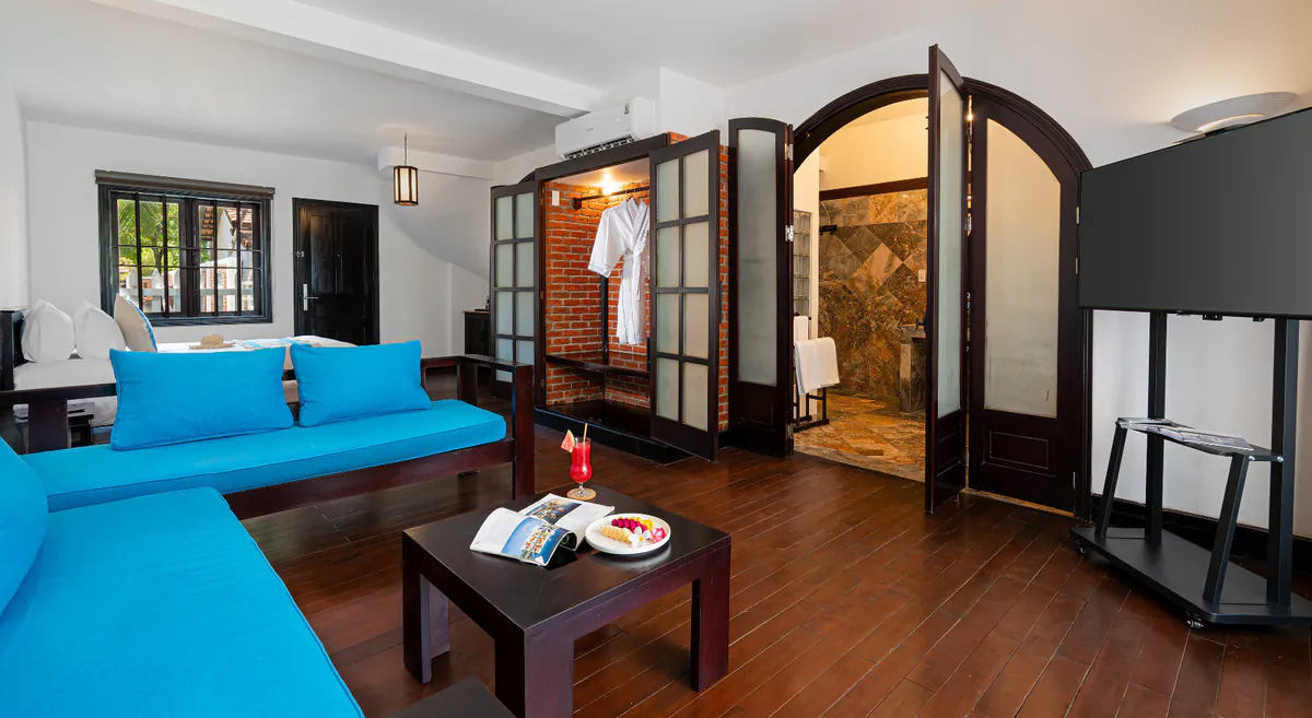 Salón con dos sofás azules y mesa baja, biombos de vidrio traslúcido y, al fondo, el hueco de ladrillo visto y el baño