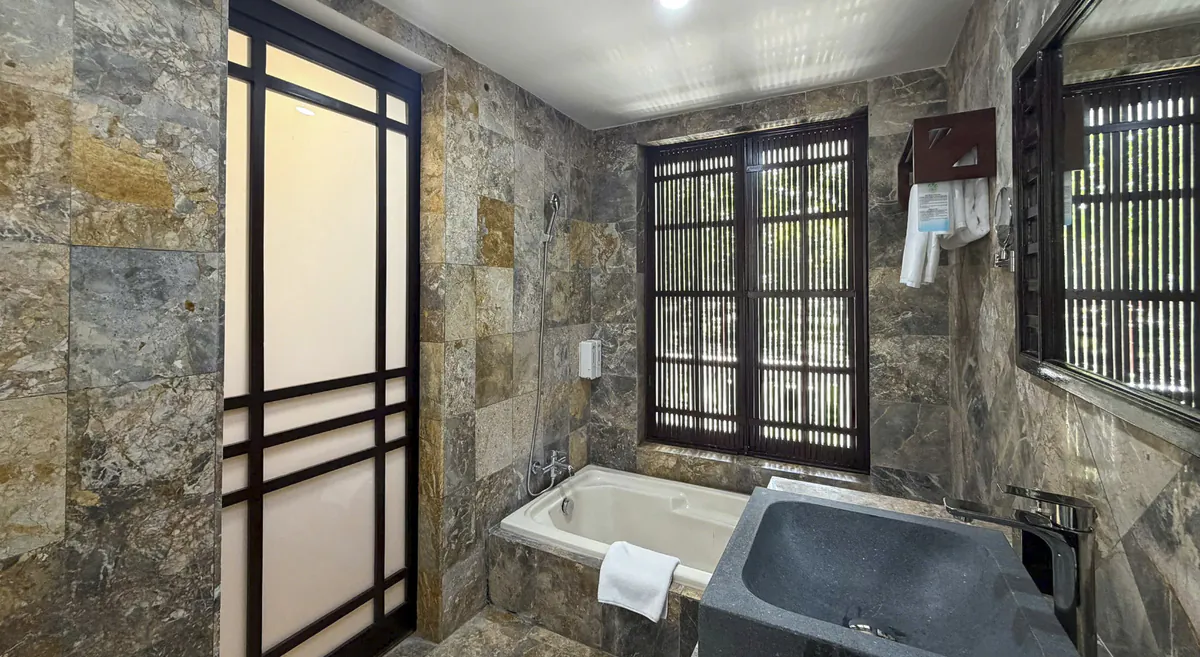 The double room's bathroom: a bath under the louvred window and a stone basin on a marble counter