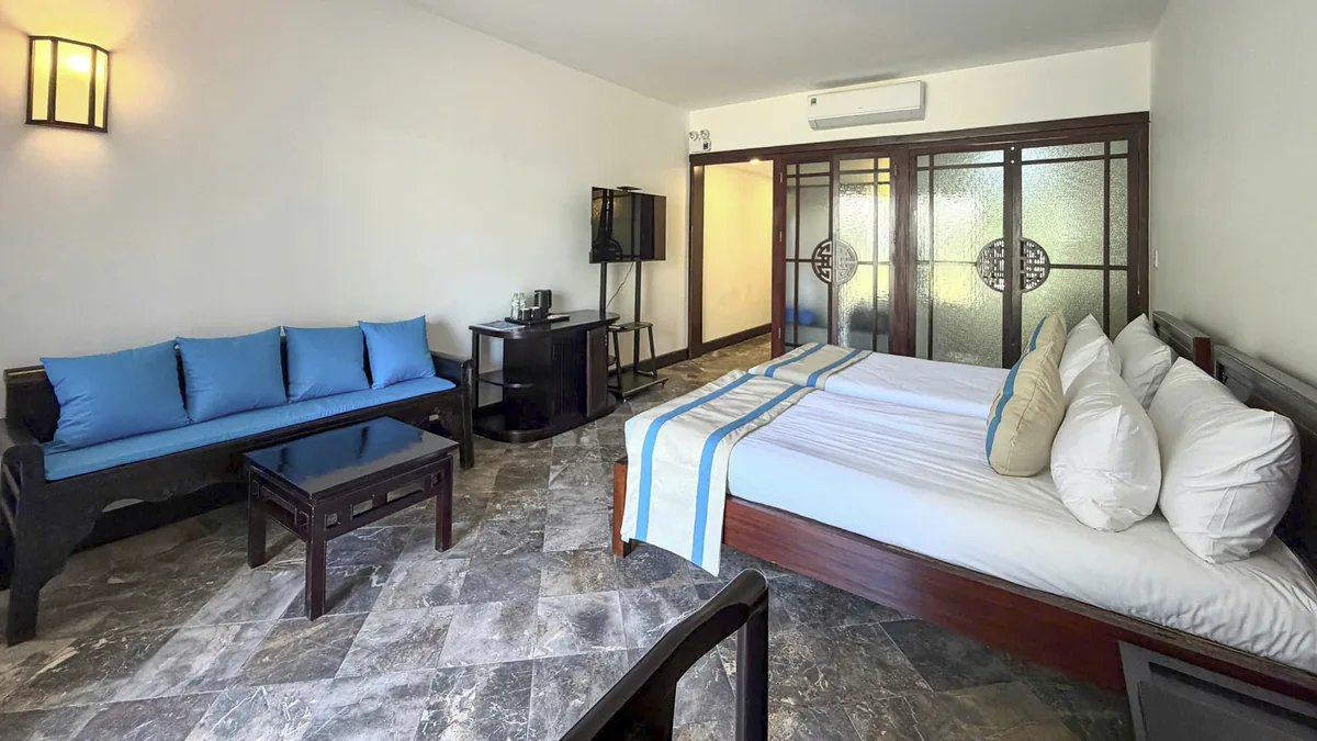 A double room with a blue-cushioned bench, a low table and the bed beyond, behind the etched-glass screens