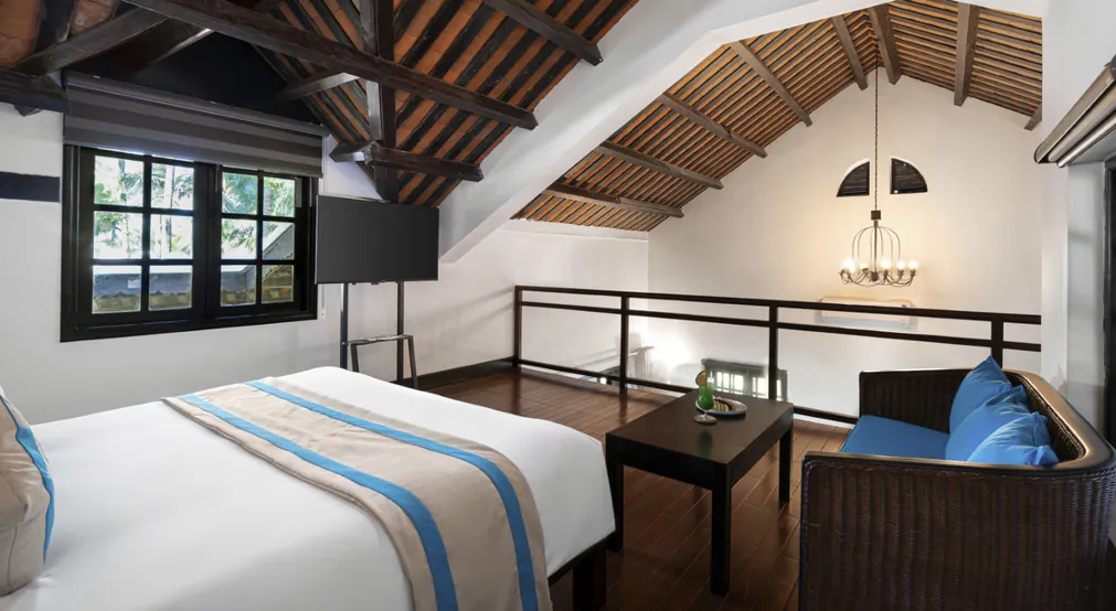 Duplex villa interior: the bed beneath the beamed roof, with the mezzanine beyond