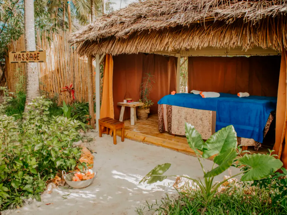 The hotel massage pavilion, with a pitched thatched roof, a couch in blue linen and a hand-painted sign