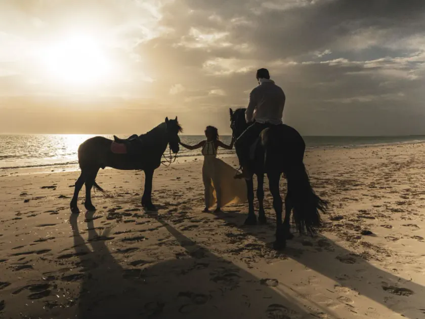 Una pareja con dos caballos en la orilla de Paje, a contraluz del atardecer