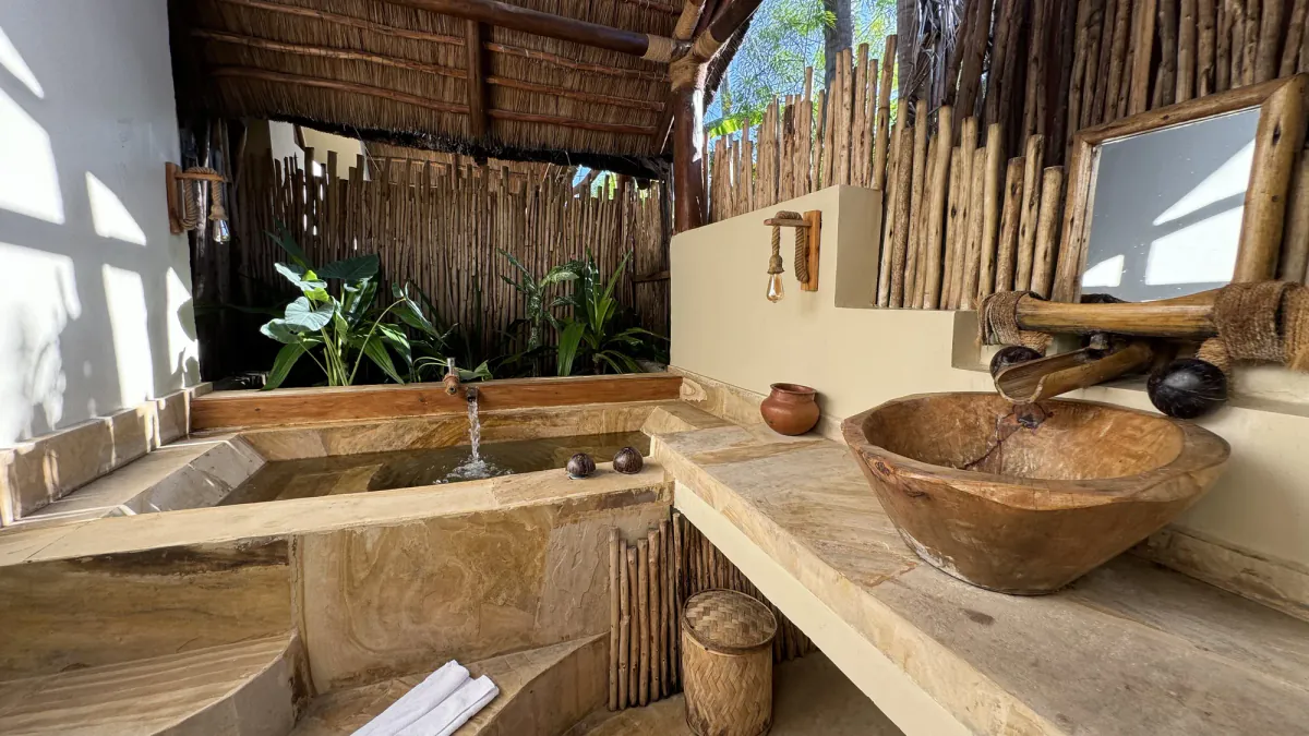 Baño al aire libre de una Poolside Villa: lavabo tallado en un tronco, cañizo y plantas