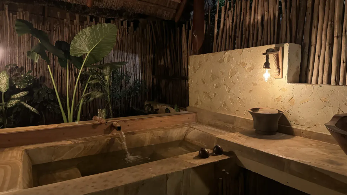 La bañera de obra del baño exterior, con plantas detrás y luz de tarde