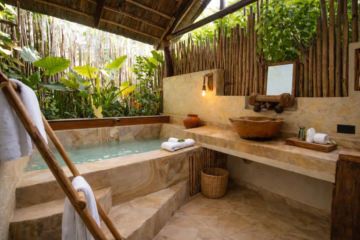 Baño exterior con una pequeña piscina de obra y el lavabo de tronco bajo el cañizo