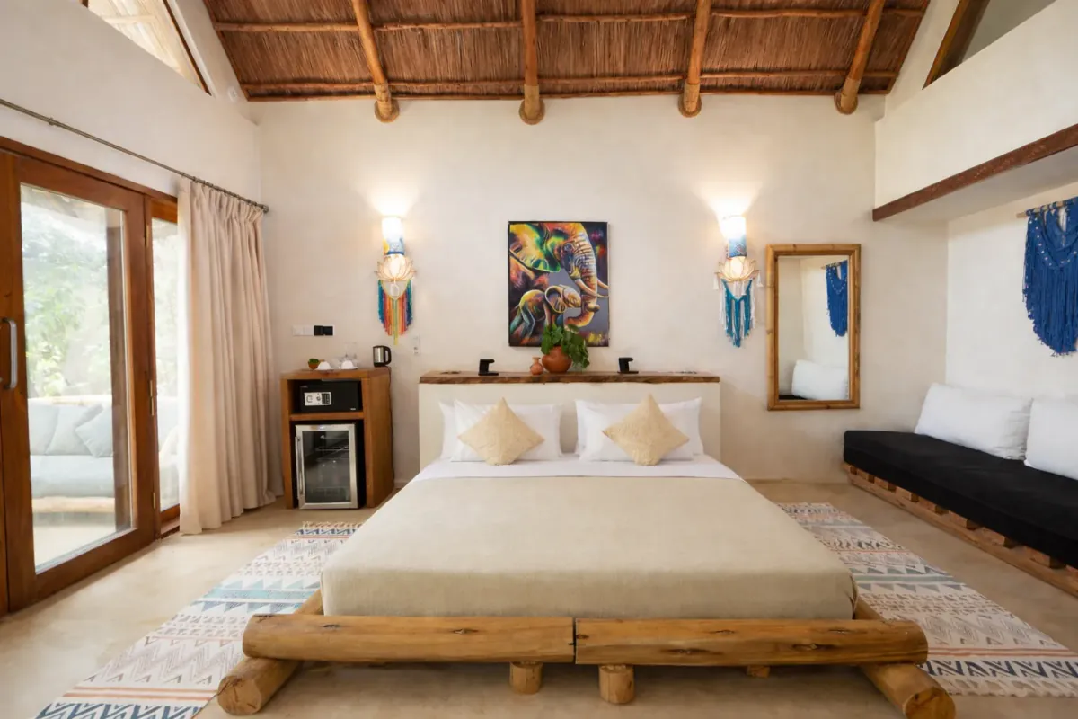 Dormitorio de una Poolside Villa bajo techo de makuti, con la cama sobre troncos y la puerta abierta al jardín
