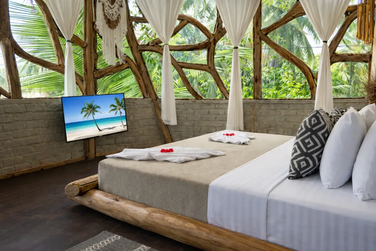 La cama de la Tree House desde el lado, con las palmas al otro lado del ventanal
