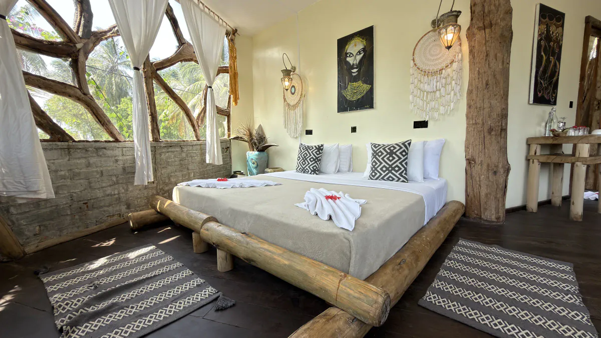 Dormitorio con ventanales de ramas, la cama sobre troncos y alfombras de rombos