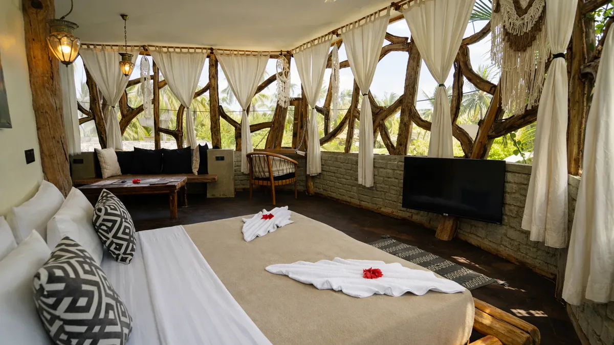Dormitorio de la Tree House del Nest: la cama king entre ventanales de ramas y cortinas blancas