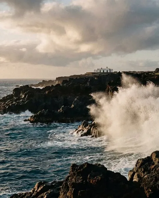 The wave breaking upward against the cliff at Los Hervideros, a small white chapel on the clifftop