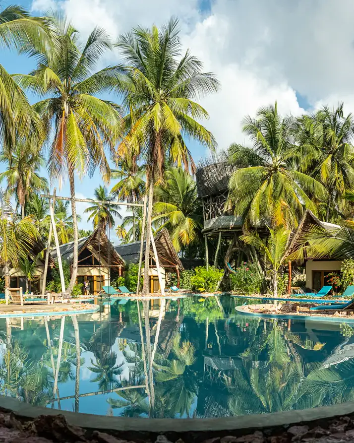 The coconut palms at The Nest mirrored top to bottom in the pool, makuti roofs showing among them