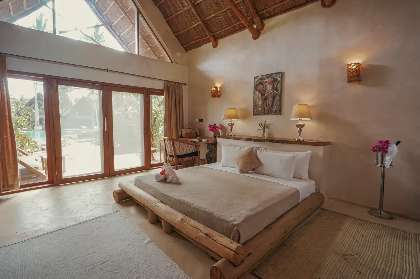 A large bedroom at The Nest under a pitched makuti roof carried on wooden beams