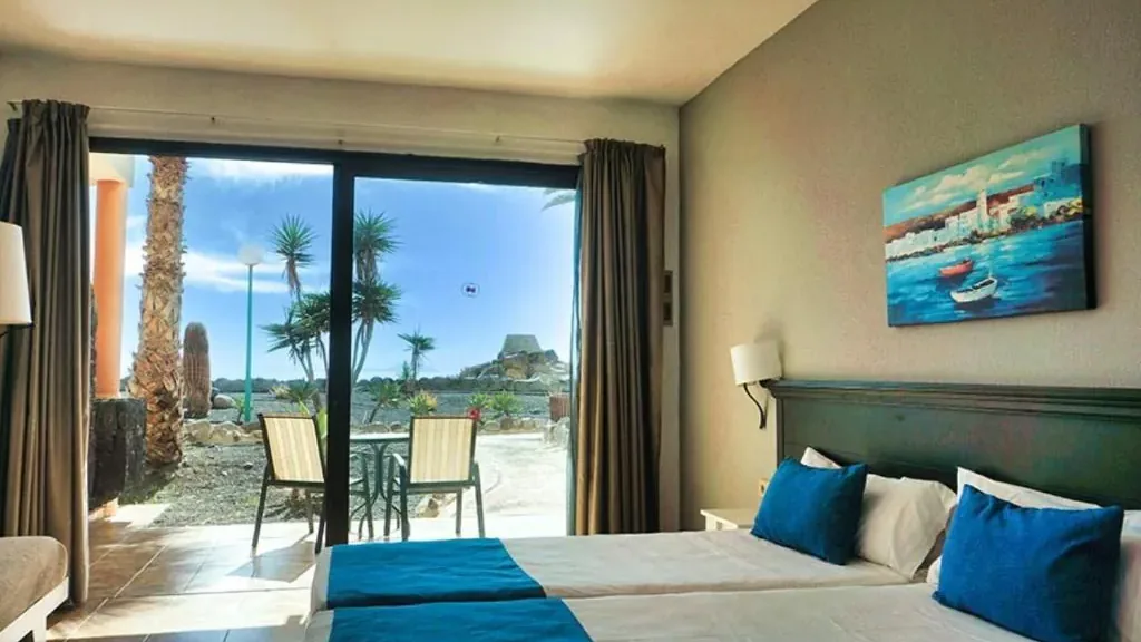 A room at the Royal Mónica with the sliding door open onto the lava-gravel garden: palms, yuccas and a rock fountain
