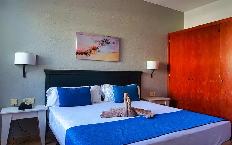 Dormitorio principal: cama de matrimonio con colcha azul, cabecero oscuro entre dos apliques y armario empotrado