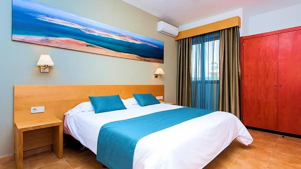 A refurbished bedroom at the Royal Mónica: beech headboard, turquoise runner, coastal panorama and red wardrobe