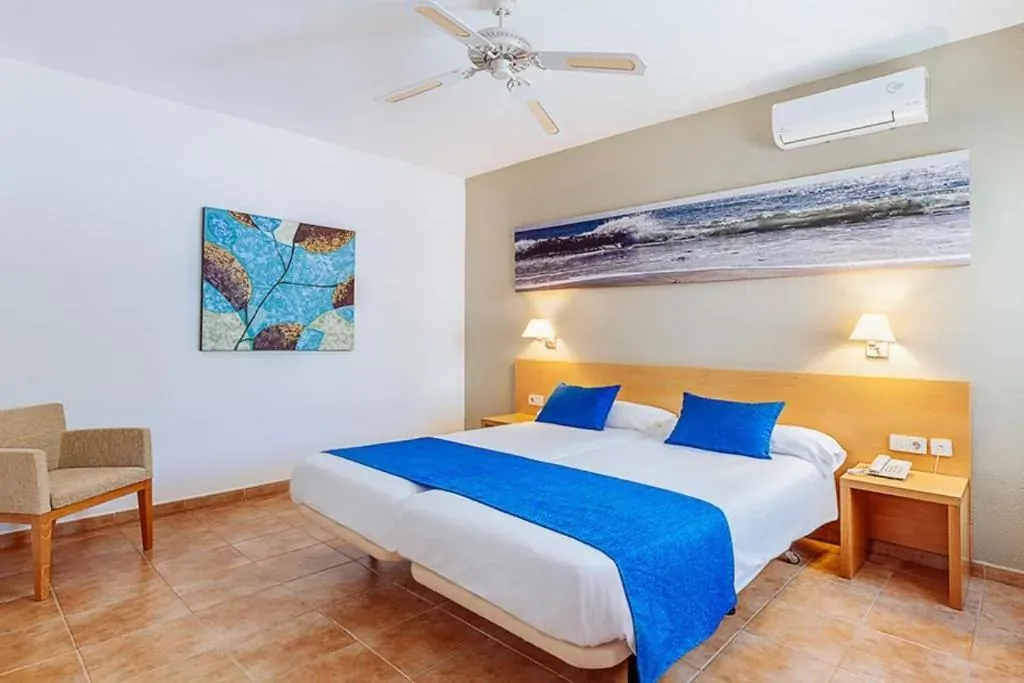 Dormitorio reformado con cabecero de haya, cojines azules, una panorámica de una ola sobre la cama y una butaca