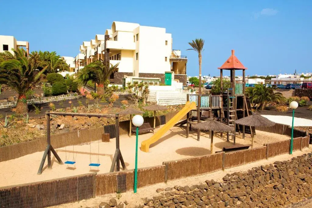 The playground at the Royal Mónica: swings, a yellow slide and a wooden tower, empty