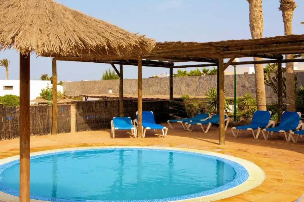 A circular pool with sun loungers and thatched parasols, ringed by a cane screen
