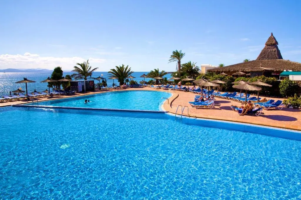 La piscina grande del hotel abierta al Atlántico, con las palmeras y el quiosco de paja al fondo