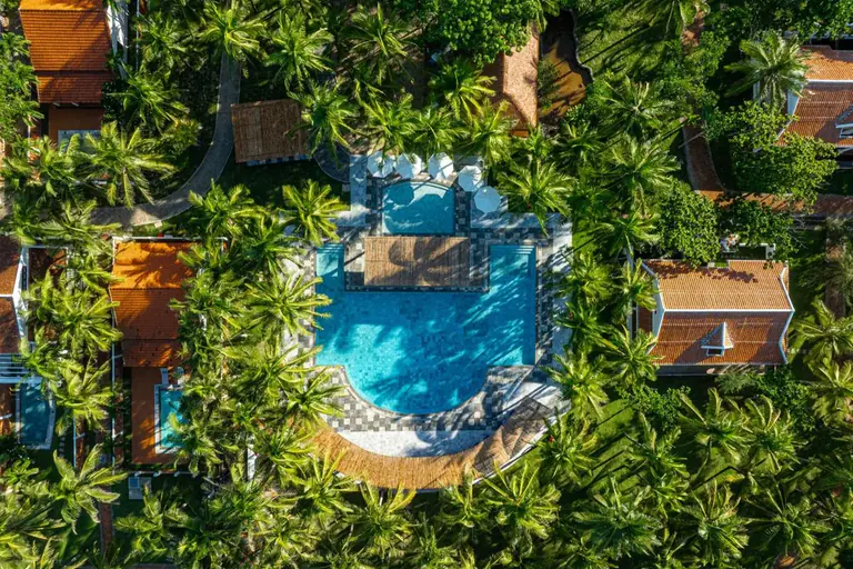 La piscina del Belhamy, cenital, entre cocoteros y tejados de teja roja