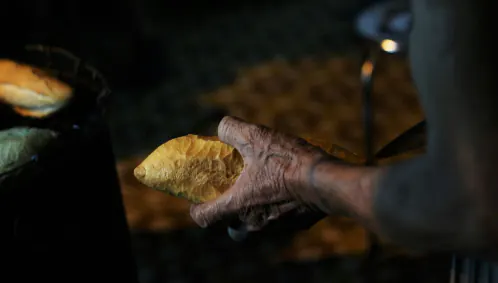 A hand holds a freshly made bánh mì, backlit over the dim stall